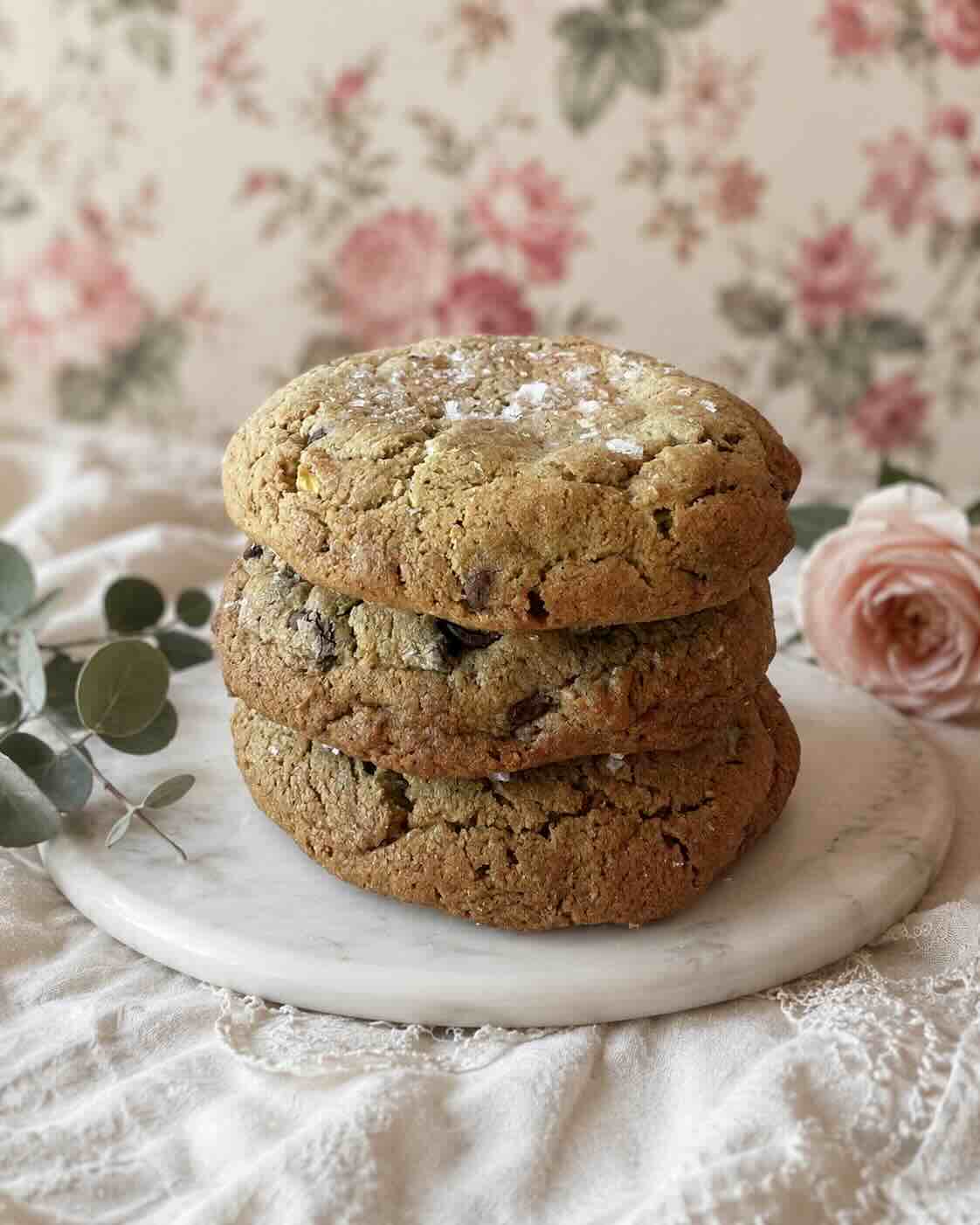 Stack of salted pistachio chocolate chip cookies on a marble board with a blush rose, SweetScape Bakery in Scottsdale